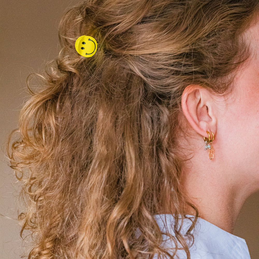 Gele smiley haarclip in krullend haar dames vrolijke haaraccessoire speels kapsel
